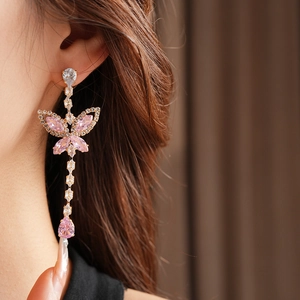 Close-up of dangling butterfly earrings with pink stones and sparkling drop pendants