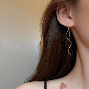 Close-up of elegant gold long tassel chain earrings with a spiral wave design on model
