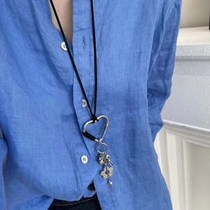 Détail d'un collier en coton noir avec mousqueton en cœur et pendentif fleur en pierre