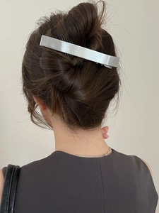 Gros plan d'une barrette en métal argenté brossé sur les cheveux châtain foncé