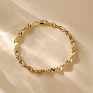 Close-up of 14K gold plated twist chain bracelet with lobster clasp on beige surface