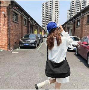 Street view of a black canvas crossbody bag with adjustable strap and casual drape