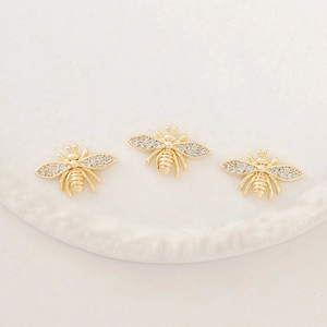 Three golden bee pendants with zircon inlay on a white textured ceramic dish