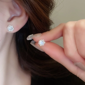 Detailed view of gold snowflake stud earrings with sparkling cubic zirconia on ear