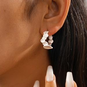 Detailed close-up of a white textured C-shaped hoop earring on a female model's ear