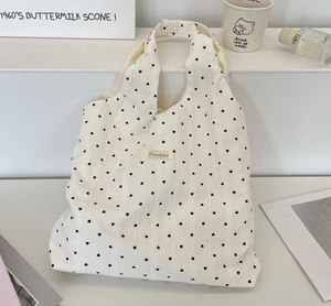 Detail der cremefarbenen Segeltuchtasche mit schwarzen Herzmotiven und Logoetikett