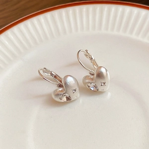 Detailed close-up of silver heart-shaped earrings with brushed metal and clear crystals