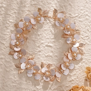 Golden bridal headband with metallic flowers and pearls on a textured beige background