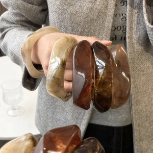 Detailed view of stacked wide resin bangles in amber tortoiseshell and beige textures