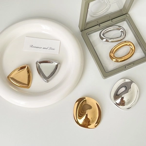 Macro shot of geometric gold and silver brooches with mirrored finish on a white tray