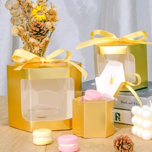 Golden hexagonal gift boxes with laser-cut windows and yellow ribbons on a wooden desk