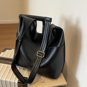 Große schwarze Leder-Einkaufstasche mit goldener Schnalle auf einem weißen Reisekoffer