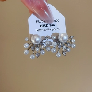 Macro shot of silver zircon pearl stud earrings with a radial firework design and tag