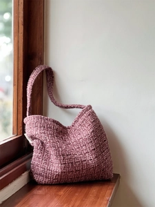 Dettaglio della trama della borsa a tracolla in tweed rosa sul davanzale in legno