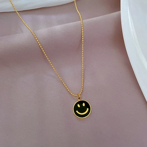 Makroaufnahme der vergoldeten Kette mit schwarzem Emaille-Smiley-Anhänger auf rosa Stoff