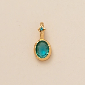 Macro shot of gold pendant with oval turquoise and blue square zircon on textured paper