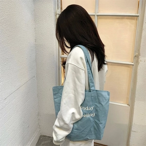 Close-up of embroidered Sunday Feeling text on a light blue denim canvas tote bag