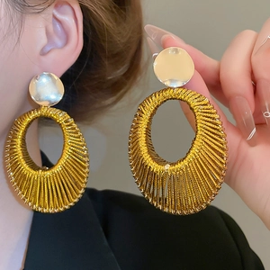 Détail de boucles d'oreilles ovales en velours tressé doré portées par un mannequin