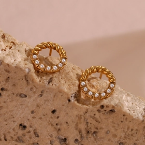 Detail of gold twisted metal hoop earring with white pearls on a natural stone surface