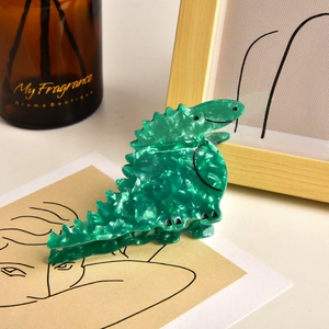 Close-up of green acetate dinosaur hair claw clip with marble texture on desk