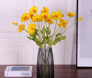 Detailed view of vibrant yellow artificial poppies in a grey fluted glass vase