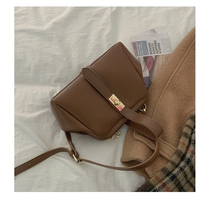 Flat lay of vintage brown crossbody bag with gold clasp on white sheet and plaid coat