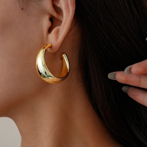 Close-up of chunky gold geometric C-shaped hoop earrings with a polished metallic finish