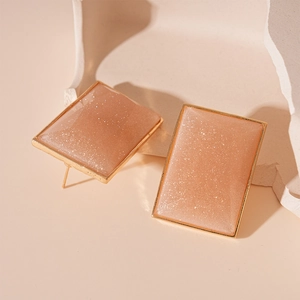 Close-up of rectangular resin earrings with champagne gold glitter and metal edges
