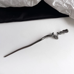 Detail view of a minimalist metal hair stick with a sleek wavy spiral design in gunmetal grey