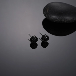 Detail shot of black stainless steel stud earrings with round star-engraved zircon stones