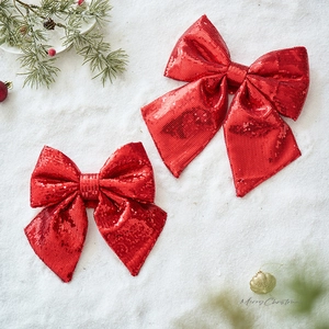 Pair of red sequined Christmas bows on a snowy background with festive holiday ornaments