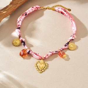 Collier en tissu rose avec pendentifs soleil cœur dorés et perles ambrées sur fond beige