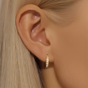 Macro side view of gold baguette-cut zircon hoop earrings worn on a female ear