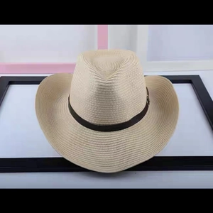 Foldable straw cowboy hat with brown leather belt buckle on a white surface