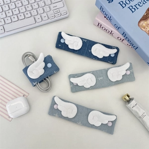 Three shades of denim fabric cable organizers with plush wings on a white desk