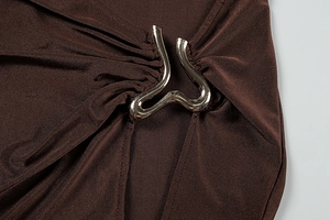 Détail de la boucle ondulée argentée sur tissu marron foncé avec plis radiaux