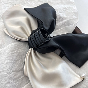 Detailed shot of a black and champagne satin bow hair clip with a pearl pendant on a white background