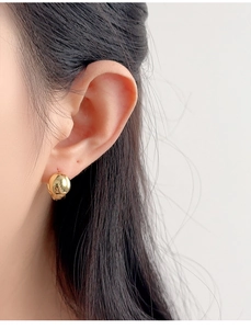 Close-up of a minimalist round gold spherical stud earring worn on a model ear