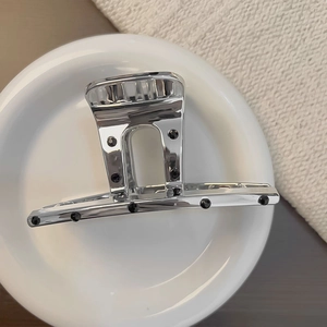 Grande pince à cheveux en métal argenté avec strass noirs sur une assiette blanche
