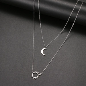 Détail du collier argenté à double couche avec pendentifs minimalistes soleil et lune
