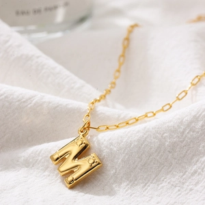 Detail of 3D bubble letter M gold necklace pendant with textured dot edges and fine chain