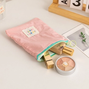 Pink fabric makeup bag with green zipper and circular ring puller showing storage space