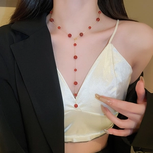 Model wearing a gold plated Y-shaped necklace with red agate beads on a white satin top