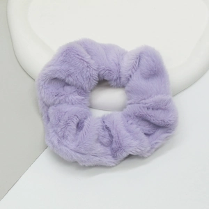Gros plan d'un chouchou en peluche violet pastel en fausse fourrure sur plateau blanc