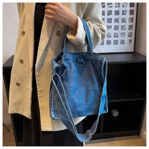 Detail of blue denim tote bag with pocket design and silver hardware worn by a model
