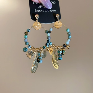Detail of 14K gold plated earrings with turquoise stones and feather charms held by hand