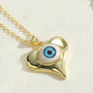Macro view of gold heart pendant with blue evil eye detail on a textured cream background
