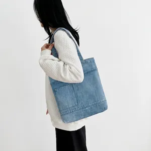 Side view of a light blue denim tote bag with square pocket worn by a model