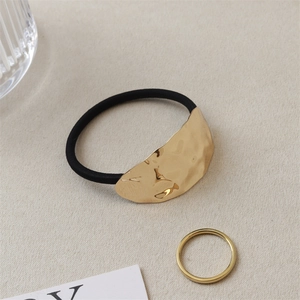 Detail of black elastic hair tie with textured hammer-finish golden metal accent piece