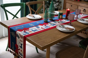 Detailed Christmas table runner with reindeer motifs and festive tassels on a wooden table